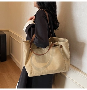 Khaki canvas tote bag detail with brown leather strap and metal rivet pocket worn by model