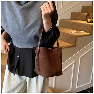 Brown frosted suede bucket bag with round buckle detail worn by a model in a retro setting