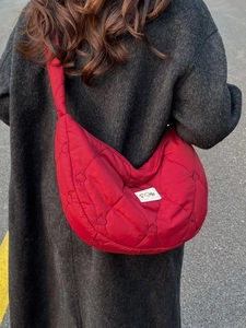 Red heart-quilted crossbody crescent bag shown on model with grey wool coat