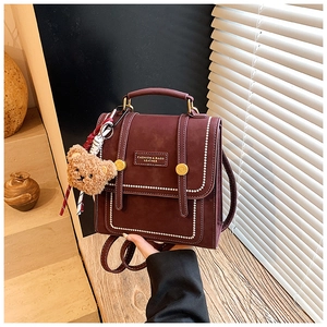 Detail of burgundy vintage backpack with white bead accents and a cute plush bear charm