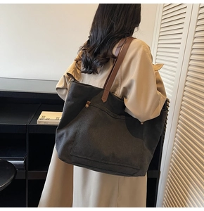 Close-up of black canvas tote bag featuring brown leather straps and vintage metal rivets