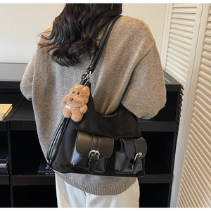 Detail of a large black tote bag with silver buckle pockets and a cute plush bear charm