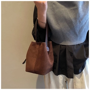Close-up of dark brown suede bucket bag with textured leather handle shown in hand