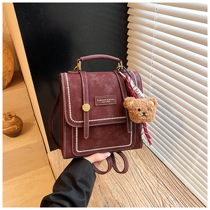 Close-up of retro burgundy leather backpack with contrast stitching and bear charm
