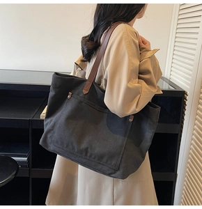 Close-up of black canvas tote bag featuring brown leather straps and rivet pocket detail