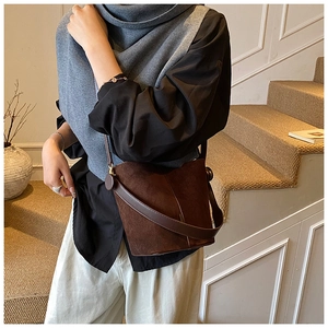 Detail of a dark brown suede bucket bag featuring a sleek metal buckle and shoulder strap