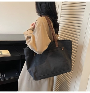 Detail of black canvas tote bag with brown straps and metal rivet pocket worn with trench coat