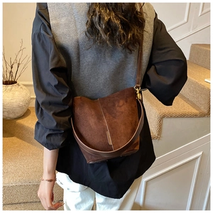 Rear view of a model wearing a brown suede bucket bag with a wide shoulder strap