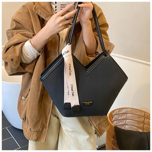 Detail of black woven tote bag featuring a V-shaped top and decorative ribbon handle