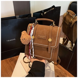 Detail of vintage brown leather backpack with white stitching and teddy bear charm