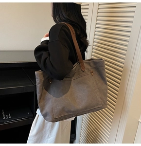 Detail of grey canvas tote bag featuring brown leather handles and reinforced stitching