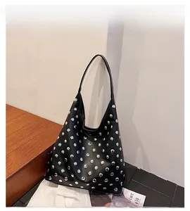 Detail view of black leather hobo bag with silver rivet studs on a wooden bench