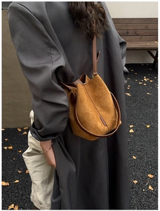 Detail of a brown suede bucket bag featuring smooth leather straps for a retro style