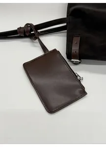 Detail of a dark brown leather mini zipper pouch with stitching on a black tote bag
