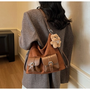 Brown suede leather tote bag with front buckle pockets and plush bear charm worn by model