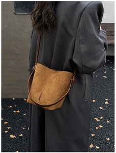 Close-up of brown suede bucket bag with leather strap and golden buckle detail