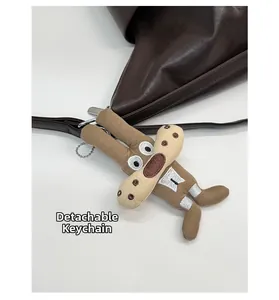 Detail of brown plush cartoon charm with silver chain on dark brown leather tote bag
