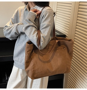 Detail of a large brown canvas tote bag with metal rivets and dual handle straps