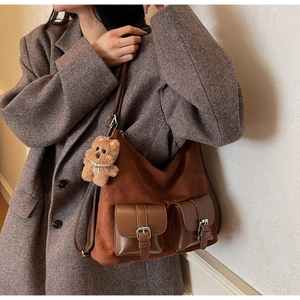 Brown suede hobo tote with dual pockets and a cute bear charm shown on a wool coat