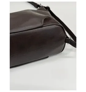 Detail of the reinforced base and adjustable strap on a dark brown synthetic tote bag