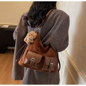Brown suede tote bag with front pockets and plush bear accessory on casual grey coat