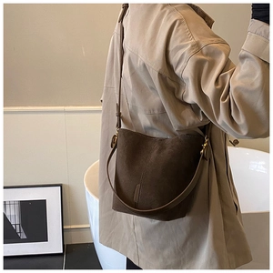 Detail of dark brown suede bucket bag worn crossbody with adjustable shoulder strap