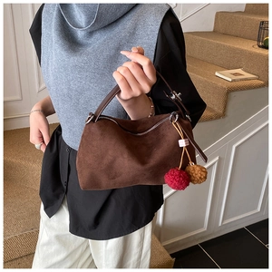 Détail d'un sac oreiller en daim marron avec un pompon en fourrure rouge et marron et zip argent