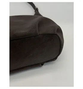 Detail view of reinforced bottom and side pleats on dark brown leather shoulder bag