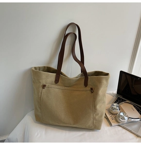Detail of khaki canvas tote bag featuring metal rivets and premium brown leather handle