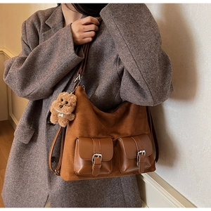 Detail view of brown faux suede tote with utility pockets and dog charm on a gray blazer