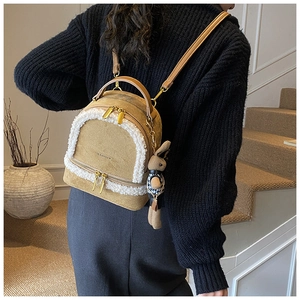Close-up of a mustard brown faux suede backpack with white fleece trim and a bunny charm