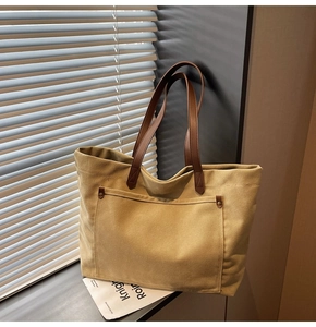 Close-up of large canvas tote bag with brown leather handles and rivet pocket detail