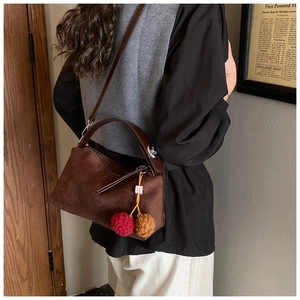 Detail of dark brown suede crossbody bag with colorful fur charms and leather straps