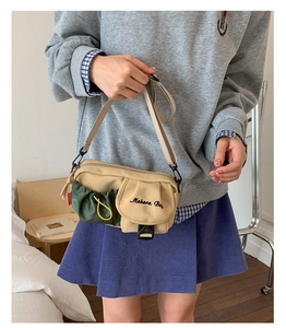 Detail of khaki and green messenger bag featuring drawstring pocket and plastic buckle