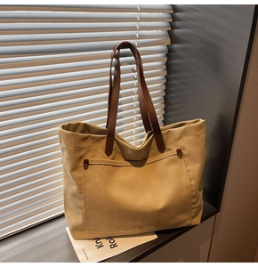 Detail view of large khaki canvas tote bag with brown leather handles and rivet pocket