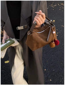 Detailed view of brown suede satchel with leather handles and decorative pom-poms