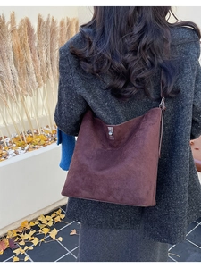 Outdoor lifestyle shot of a large burgundy suede bucket bag on a model's shoulder