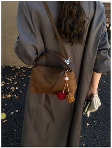 Detail of dark brown suede pillow bag with colorful cherry charms on a grey trench coat