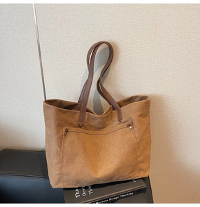 Detail of caramel canvas tote bag with front pocket, metal rivets and leather shoulder strap