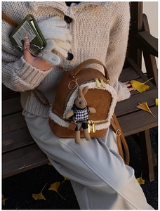 Detail of a brown suede mini backpack with white faux fur trim and a cute rabbit charm