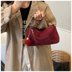 Detail of burgundy suede handbag with plush ball pendant shown on a trench coat