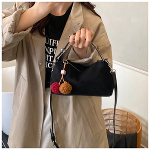 Detail of black suede pillow bag with colorful plush ball charms and silver zipper
