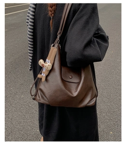 Detail of coffee brown leather tote bag with a plush bunny charm on outdoor background