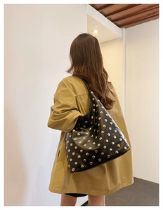 Detail shot of a black hobo bag with silver rivet studs worn by a model in a khaki jacket