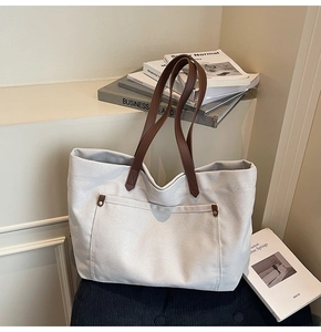 Detail of grey canvas tote bag with brown leather straps and metal rivets on a chair