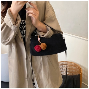 Black suede pillow bag with cherry plush charm shown on a trench coat model