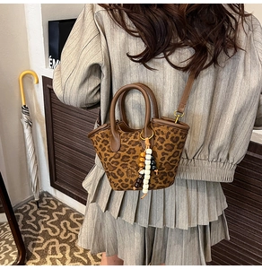 Detail of leopard print bucket bag featuring leather trim and beaded charm on model