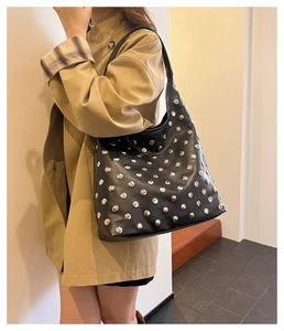 Detail of black leather hobo bag with silver rivets worn over a stylish trench coat