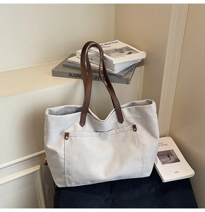 Detail view of canvas tote bag with brown leather straps and front buckle pocket
