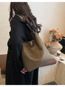 Detail of a dark brown suede bucket bag with silver twist lock and wide shoulder strap